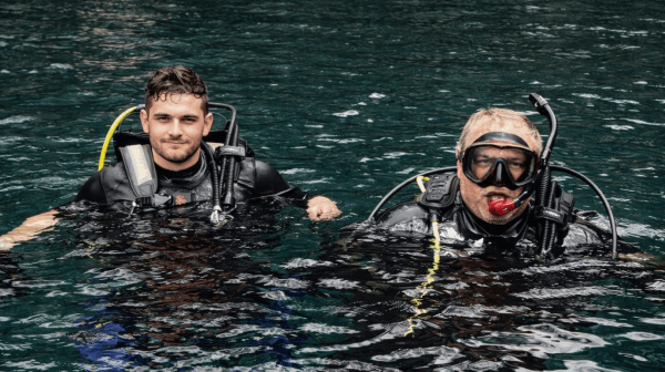Two divers in wetsuits and gear floating in clear blue water.