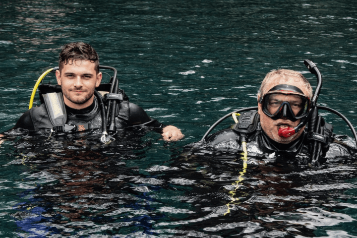 Two divers in wetsuits and gear floating in clear blue water.