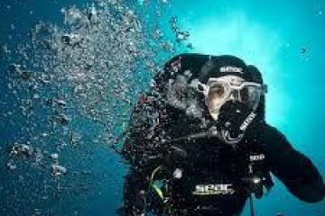 Scuba diver underwater with bubbles rising in bright blue ocean.