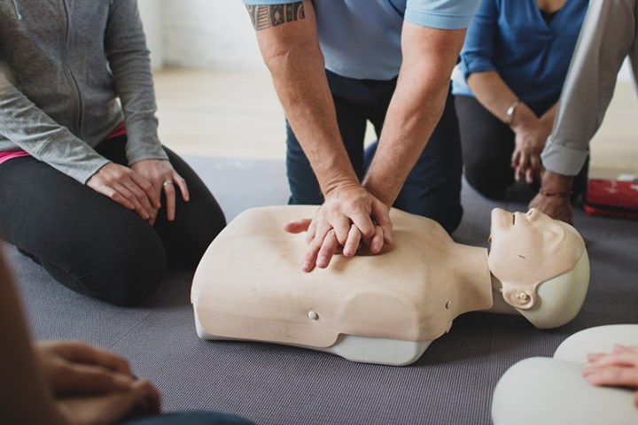 Person demonstrating CPR on a mannequin surrounded by onlookers.