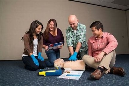 Four people practicing CPR on a dummy with training materials on the floor.