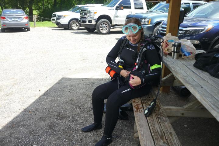 Person in scuba gear sitting on a bench near parked cars, preparing equipment.