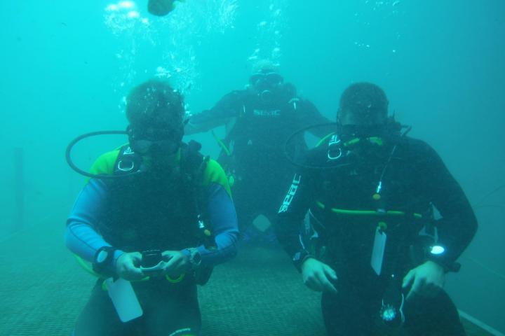 Three scuba divers underwater wearing full gear on a submerged platform.