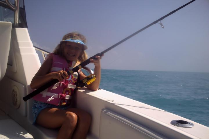 Child wearing a life jacket and visor, fishing on a boat in the ocean.