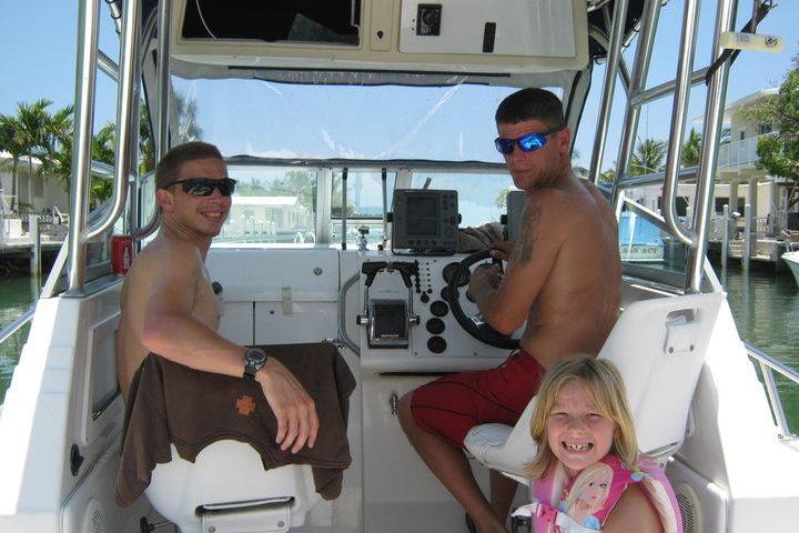 Two men and a child on a boat, one man steering, all under a sunny sky.