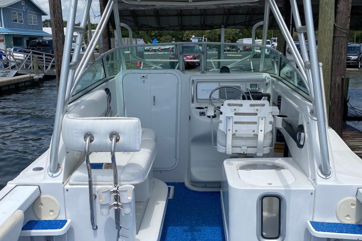 Interior of a boat with blue flooring, white seats, and a steering console.