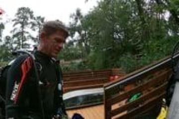 Person in diving gear near wooden railing with trees in background.