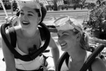 Two women with diving gear smiling by a pool.
