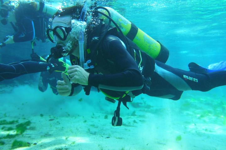 Two scuba divers underwater with tanks and gear, giving thumbs up.