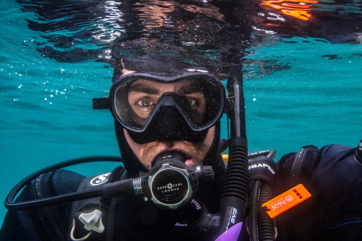 Scuba diver underwater with mask and regulator, reflection on water surface.