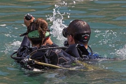 Two divers in wetsuits and masks, with scuba gear, preparing to dive in open water.