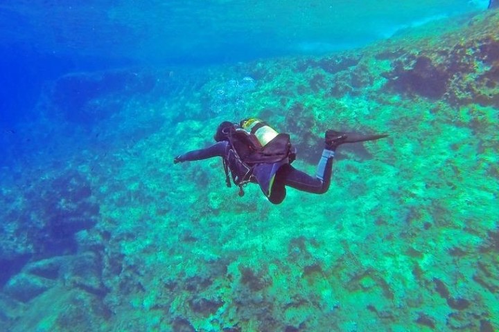Scuba diver swimming over a vibrant coral reef in clear blue water.