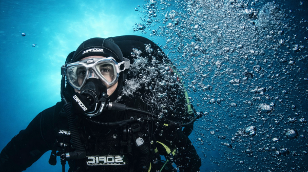 Diver underwater with scuba gear, surrounded by bubbles in clear blue water.