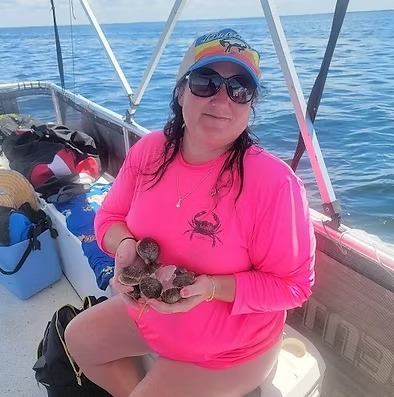 Person on a boat in pink shirt and cap holding a handful of shells, with ocean in the background.