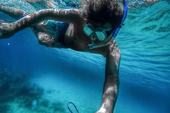 Person snorkeling underwater in clear blue ocean wearing mask and snorkel.