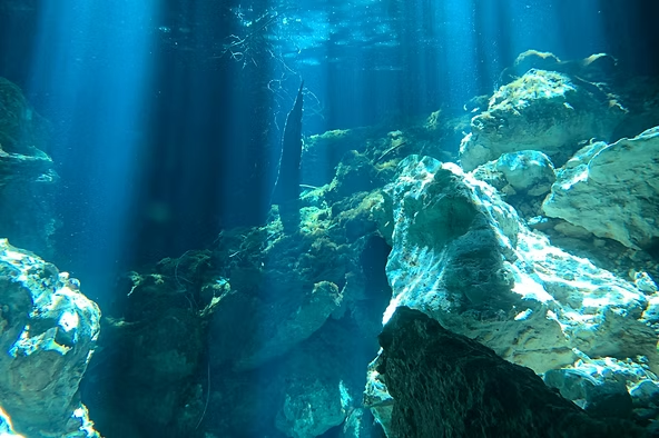 Underwater scene with rocks and sun rays penetrating through clear water.