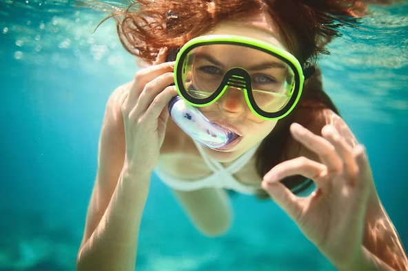 Woman underwater with snorkel and mask making OK gesture.