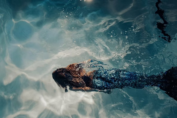 Underwater view of a person wearing a mermaid tail swimming in a pool.